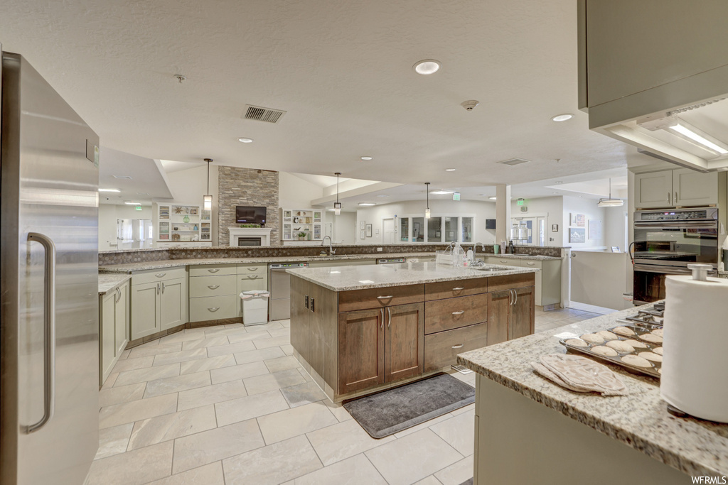 kitchen featuring a center island, stainless steel oven, refrigerator, TV, dishwasher, light tile floors, and light stone countertops