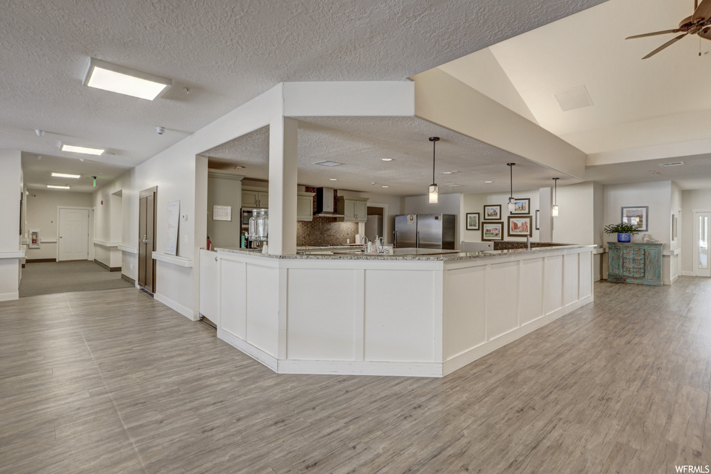 kitchen featuring a ceiling fan, exhaust hood, stainless steel refrigerator, pendant lighting, light countertops, and light hardwood flooring