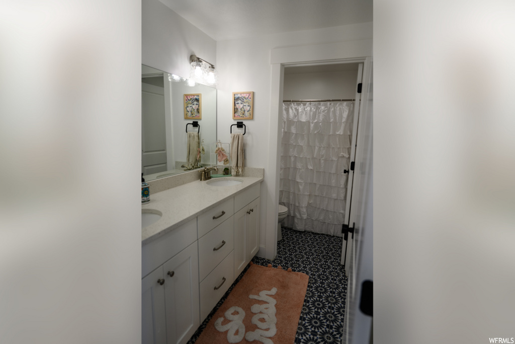 bathroom with toilet, shower curtain, his and hers vanity, and mirror