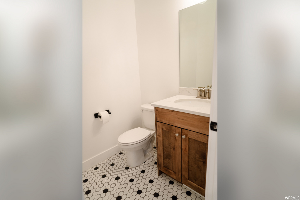 half bathroom featuring tile floors, toilet, and vanity
