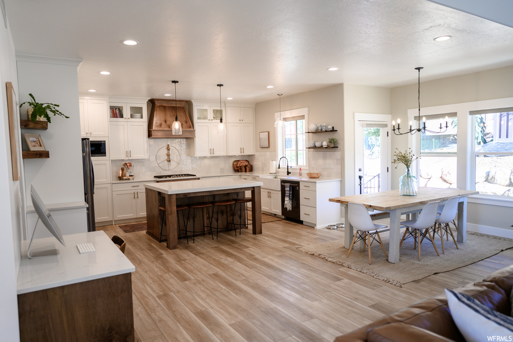 kitchen featuring natural light, a kitchen island, refrigerator, exhaust hood, dishwasher, pendant lighting, light countertops, and light hardwood floors