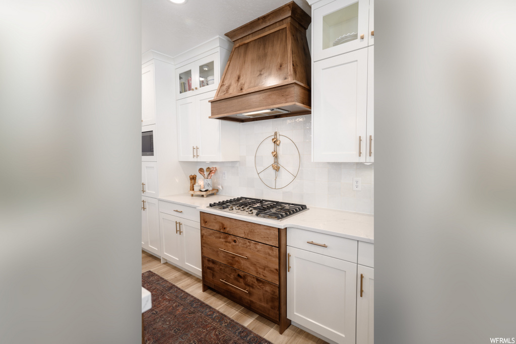kitchen featuring gas stovetop, ventilation hood, light countertops, and white cabinetry