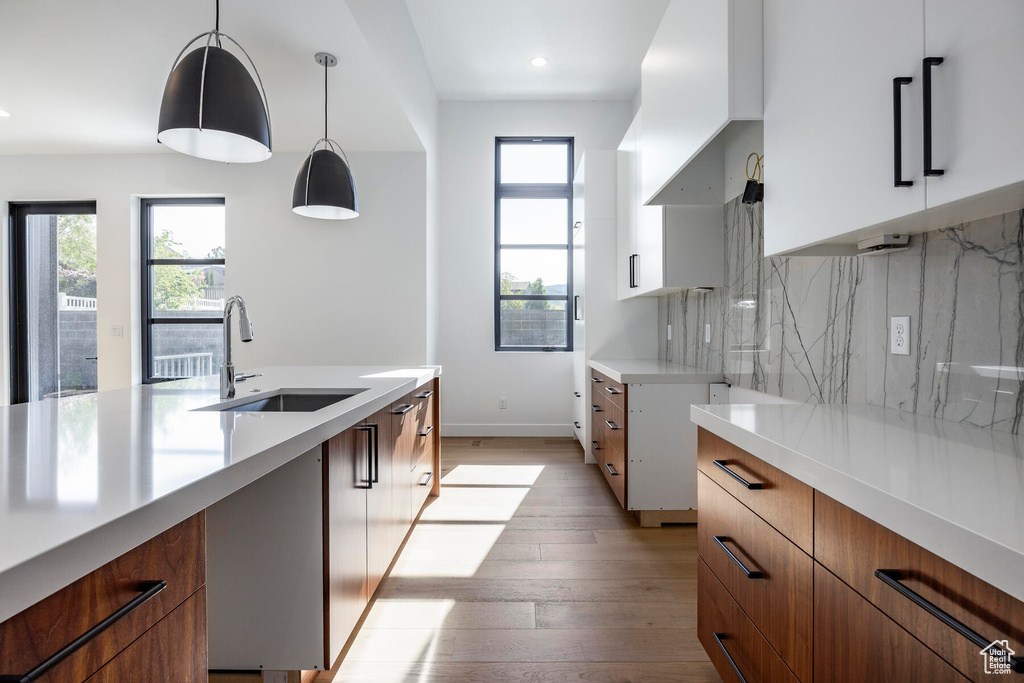 Kitchen with decorative light fixtures, tasteful backsplash, white cabinets, sink, and light wood-type flooring