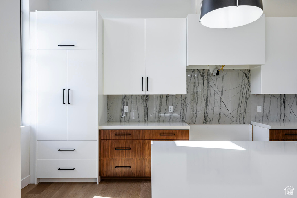 Kitchen with tasteful backsplash, hardwood / wood-style flooring, and white cabinetry