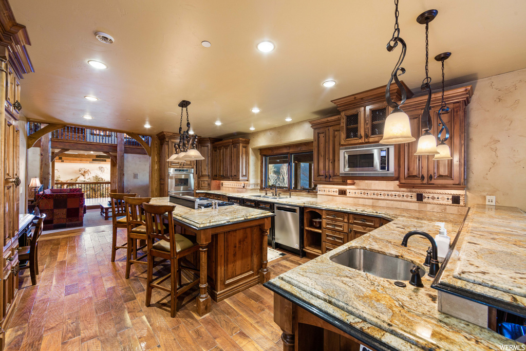 kitchen with a healthy amount of sunlight, a center island, a breakfast bar area, microwave, dishwasher, oven, pendant lighting, light granite-like countertops, and light hardwood floors