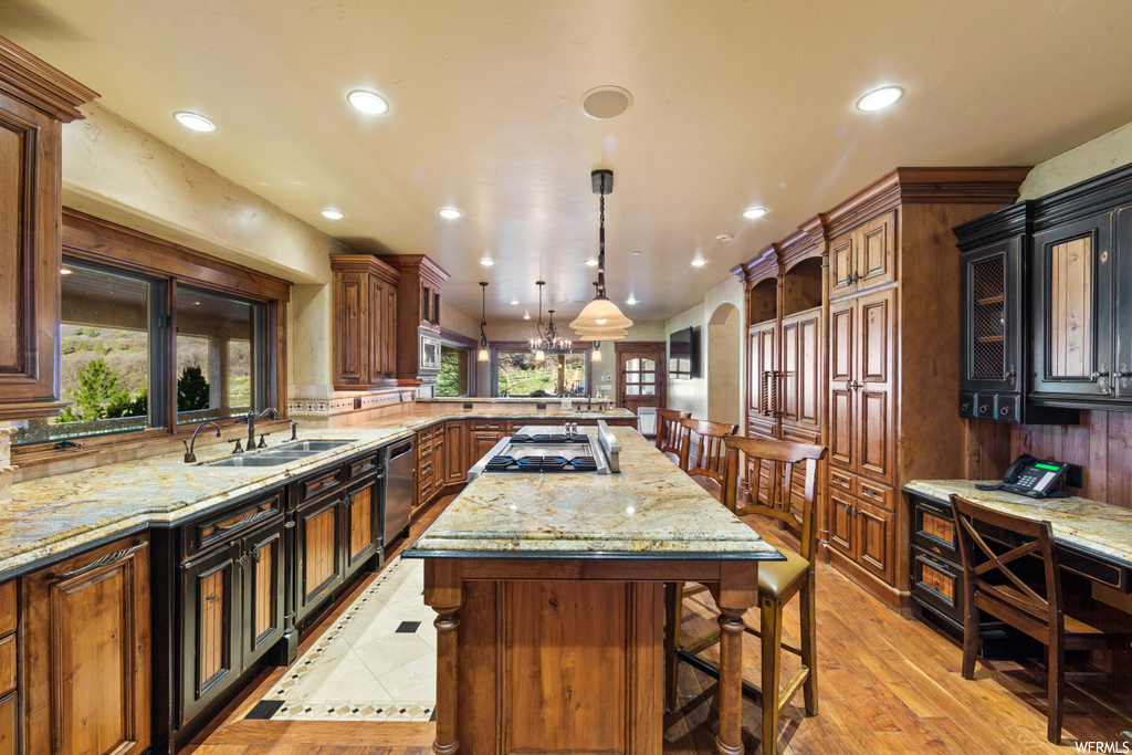 kitchen featuring a center island, a breakfast bar area, gas cooktop, dishwasher, pendant lighting, light granite-like countertops, and light parquet floors