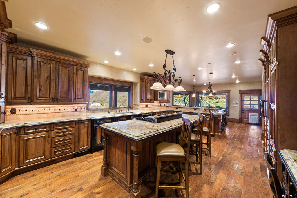 kitchen with a kitchen breakfast bar, a center island, natural light, light stone countertops, light hardwood floors, and dark brown cabinets