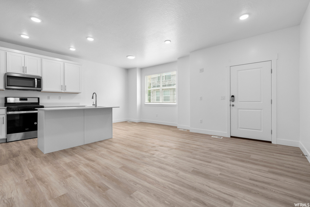 kitchen with natural light, range oven, microwave, light parquet floors, and white cabinetry