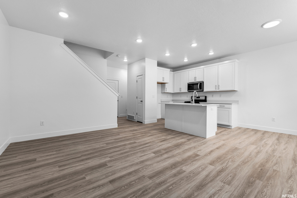 kitchen featuring microwave, white cabinetry, light countertops, and light hardwood flooring