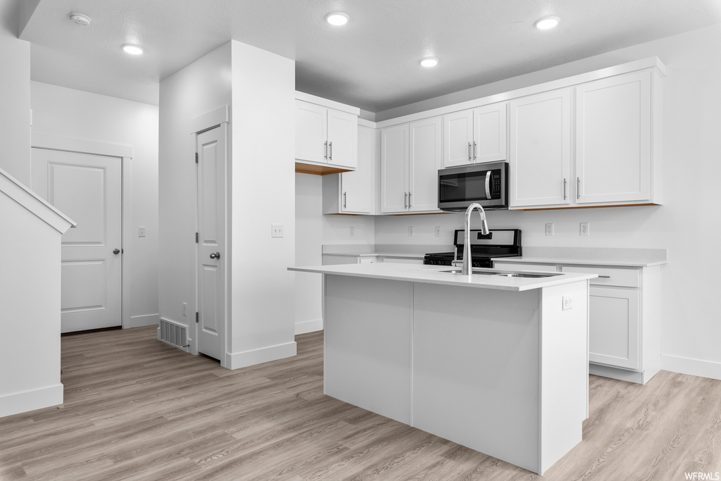 kitchen featuring range oven, microwave, white cabinets, light countertops, and light hardwood floors