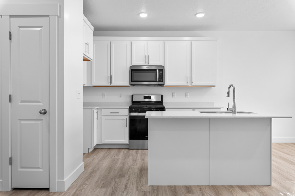 kitchen featuring range oven, microwave, white cabinets, light countertops, and light hardwood flooring