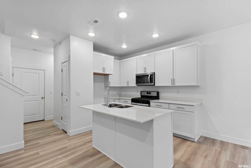 kitchen featuring range oven, microwave, light countertops, white cabinets, and light parquet floors