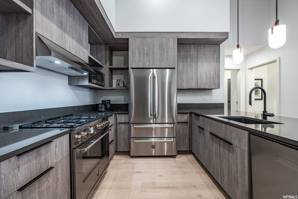kitchen featuring refrigerator, gas range oven, range hood, dishwasher, pendant lighting, light hardwood floors, and dark countertops
