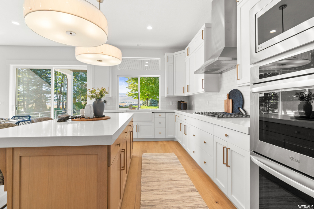 Kitchen with light hardwood / wood-style flooring, a kitchen island, wall chimney range hood, backsplash, and white cabinetry