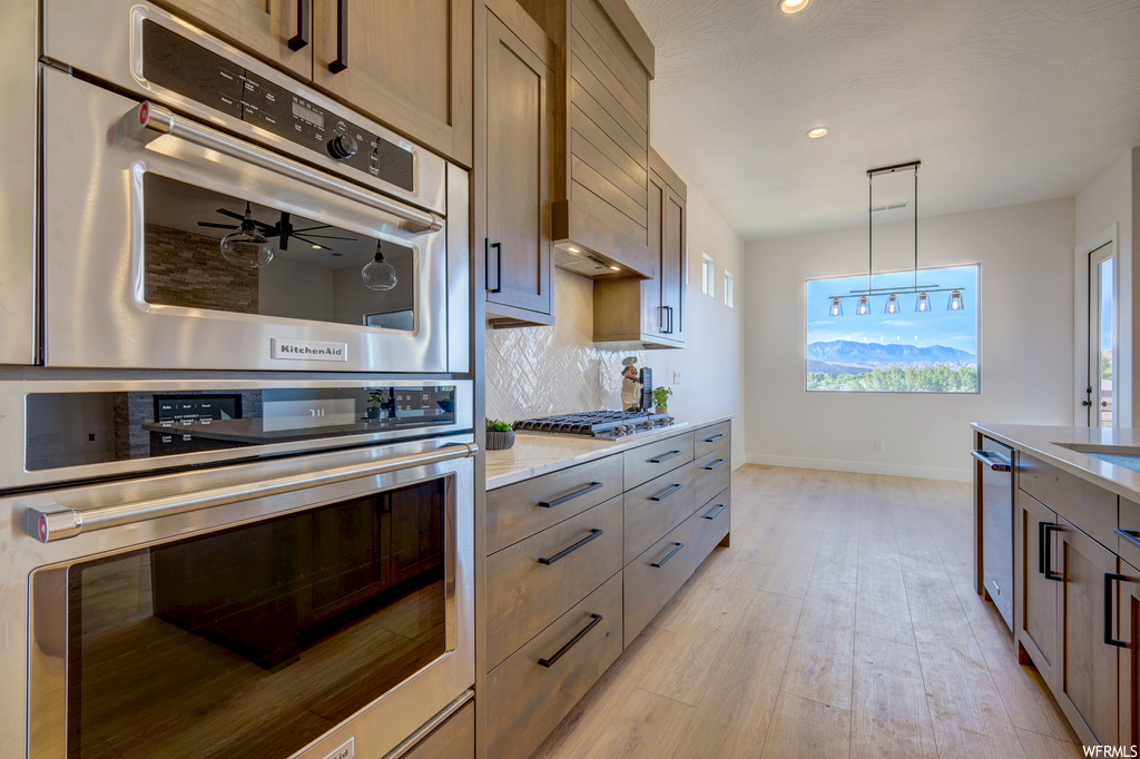 Kitchen featuring gas stovetop, double oven, pendant lighting, light flooring, and light granite-like countertops