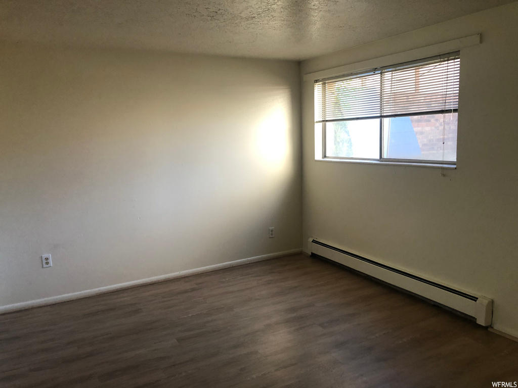 hardwood floored spare room with natural light and baseboard radiator
