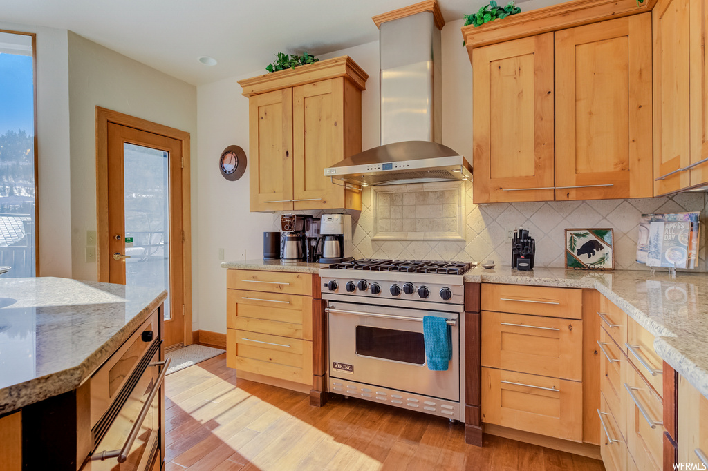 kitchen featuring natural light, extractor fan, stainless steel finishes, gas range oven, light countertops, brown cabinetry, and light hardwood floors