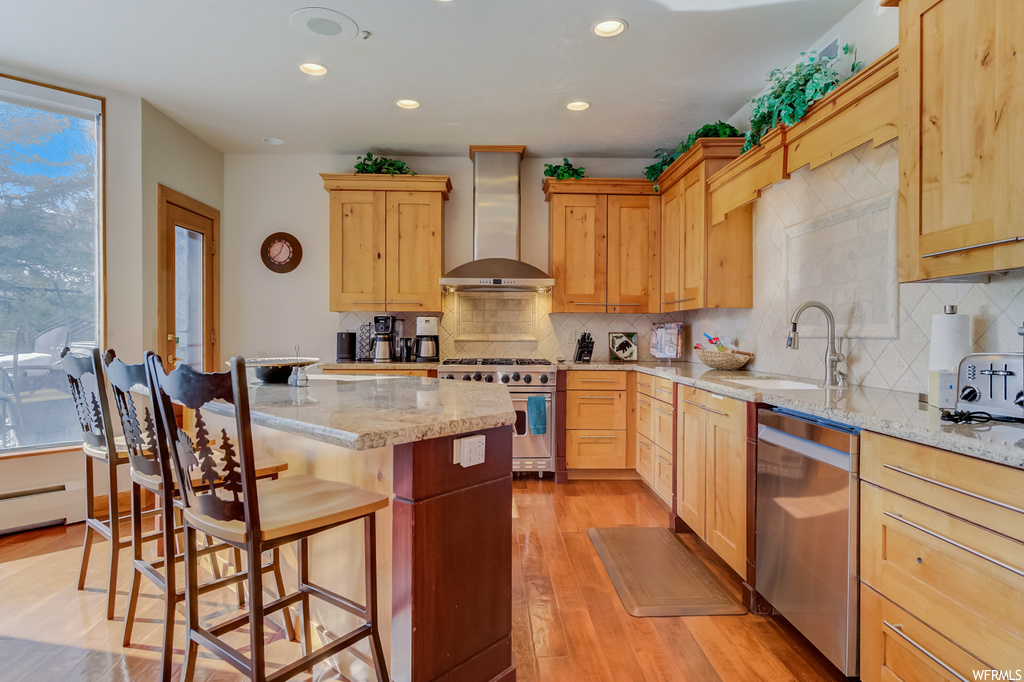 kitchen with a kitchen bar, natural light, stainless steel dishwasher, exhaust hood, gas range oven, brown cabinets, light stone countertops, and light hardwood flooring