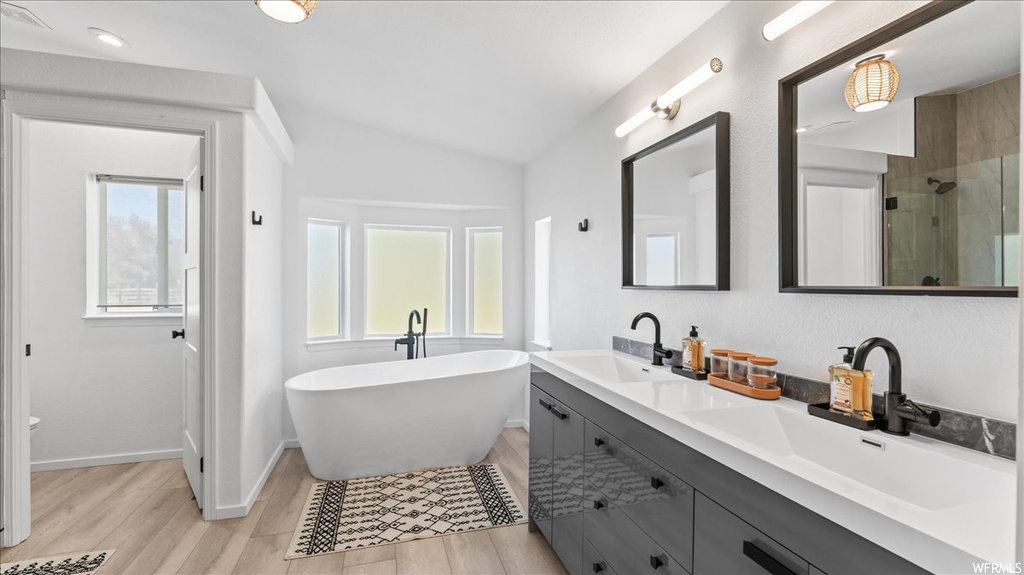 Bathroom featuring plenty of natural light, double sink vanity, lofted ceiling, and independent shower and bath