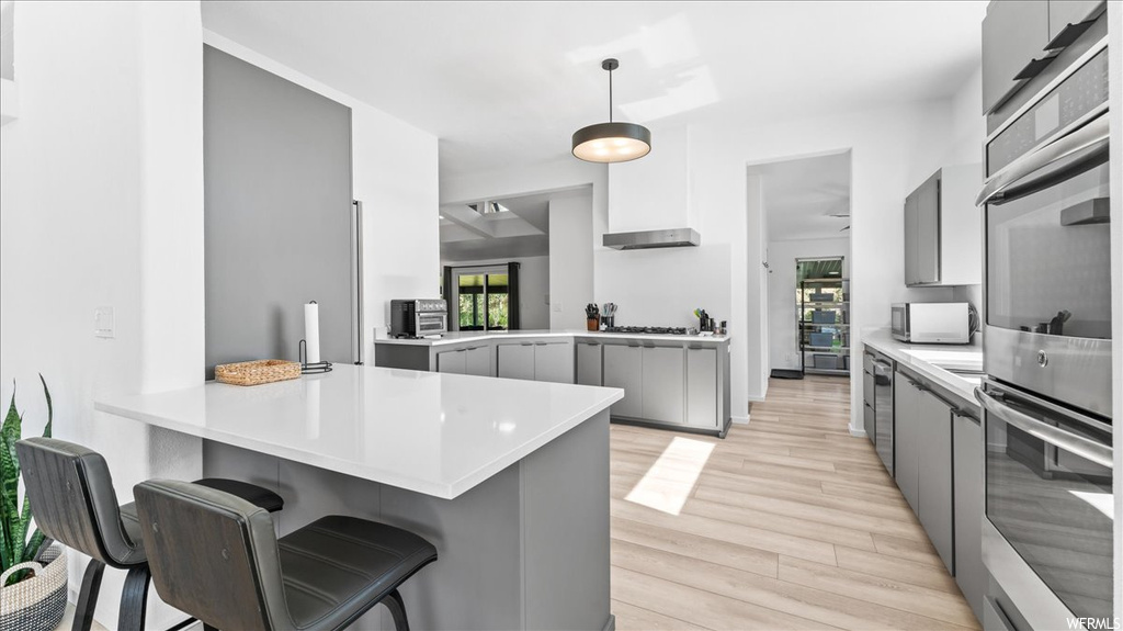 Kitchen featuring a breakfast bar area, gray cabinets, light hardwood / wood-style flooring, and pendant lighting