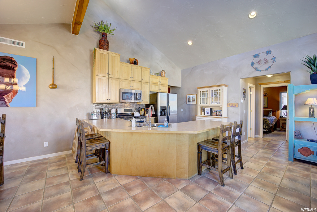 kitchen featuring a kitchen breakfast bar, vaulted ceiling, refrigerator, range oven, stainless steel microwave, light countertops, light brown cabinets, and light tile flooring
