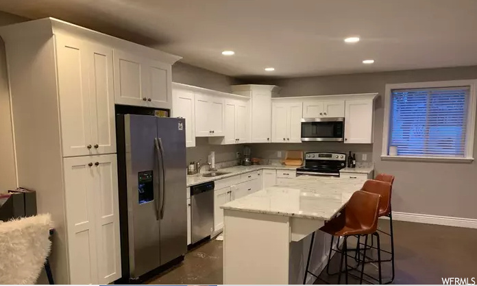 kitchen with a kitchen breakfast bar, refrigerator, range oven, stainless steel microwave, dishwasher, dark flooring, white cabinetry, and light countertops