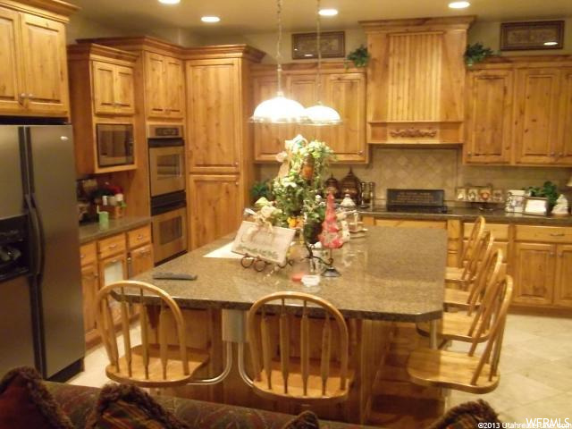 kitchen with tile flooring, a breakfast bar area, double oven, refrigerator, microwave, pendant lighting, dark stone countertops, and brown cabinets