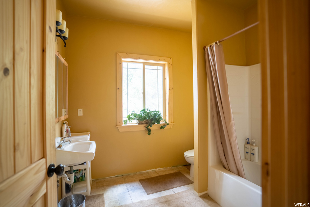full bathroom with natural light, tile flooring, toilet, washbasin, shower curtain, mirror, and washtub / shower combination