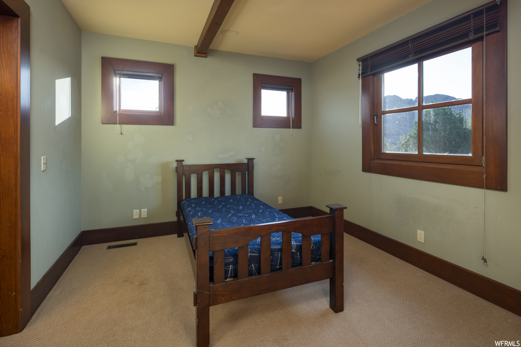bedroom featuring carpet, beamed ceiling, and natural light