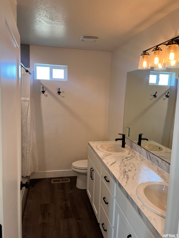 Bathroom with a textured ceiling, double vanity, dark hardwood floors, and mirror