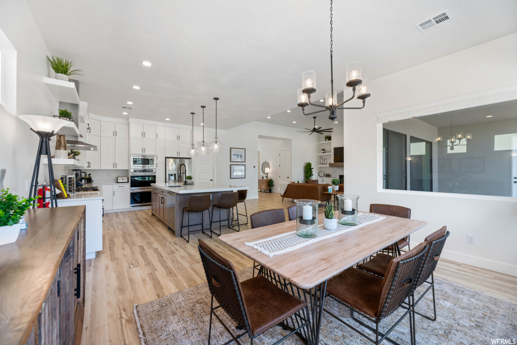 wood floored dining area with a breakfast bar, ceiling fan with chandelier, and stainless steel microwave