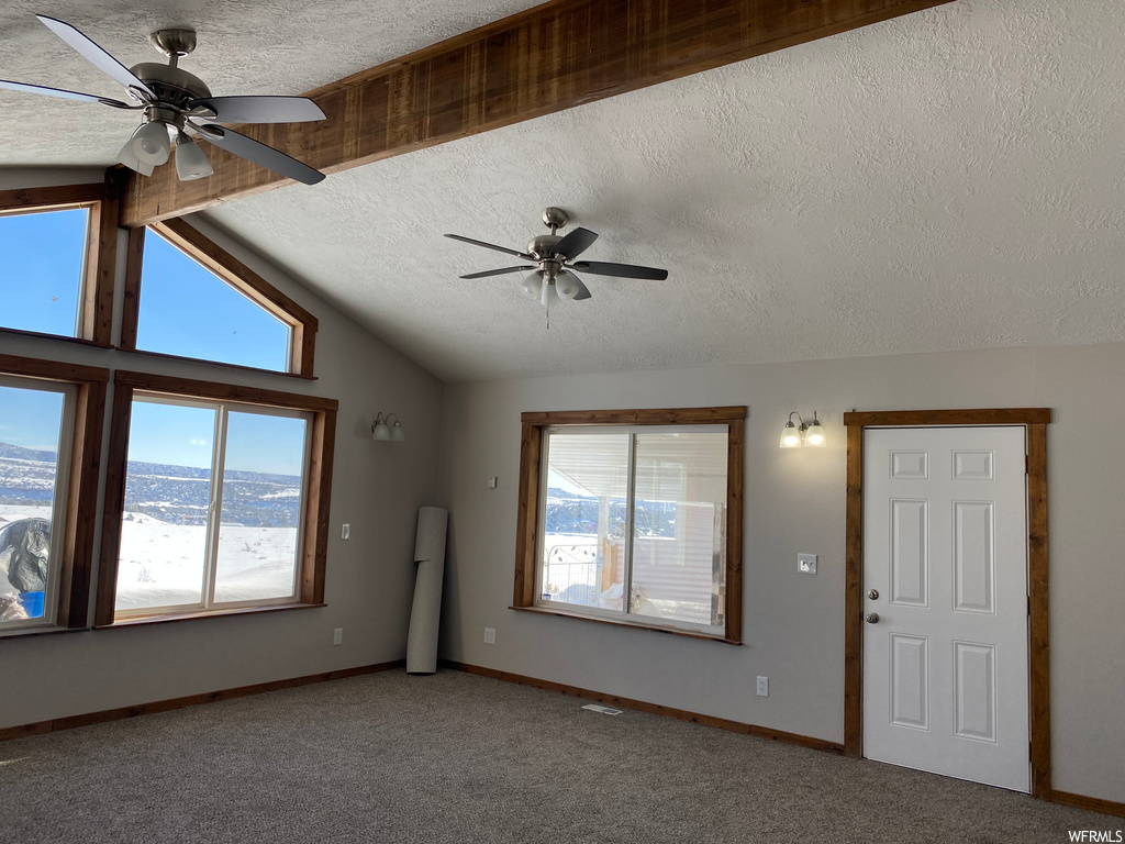 empty room with carpet, lofted ceiling with beams, a ceiling fan, and natural light