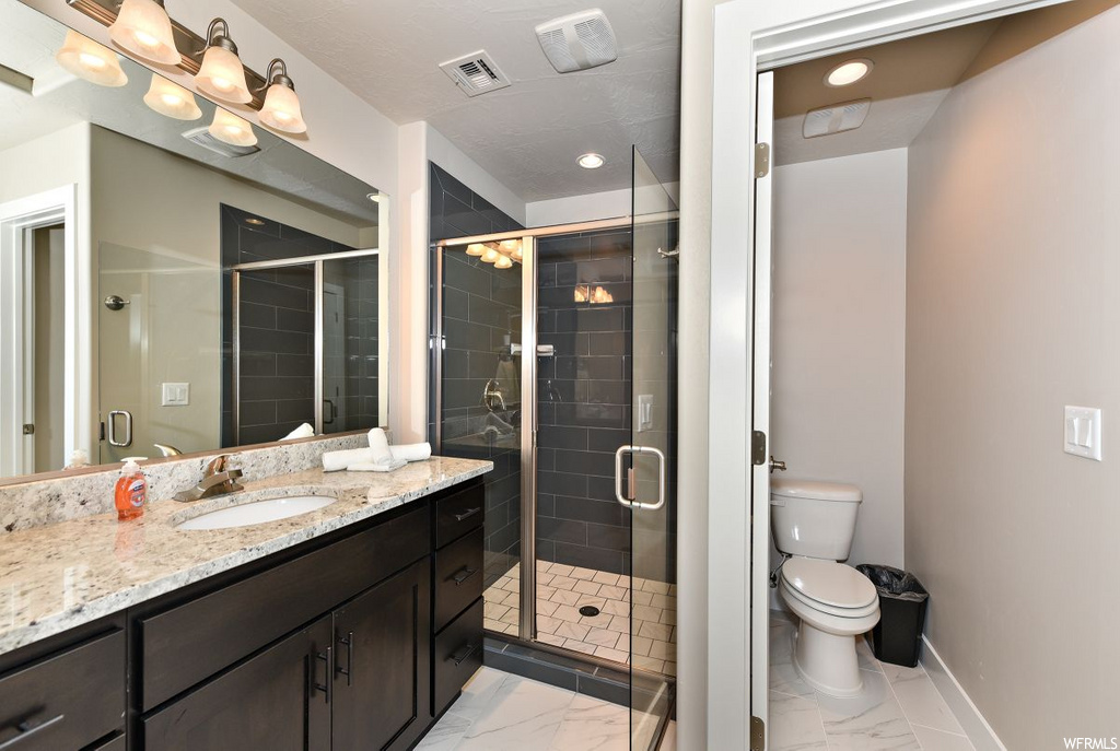 full bathroom featuring tile flooring, mirror, toilet, vanity with extensive cabinet space, and shower with glass door