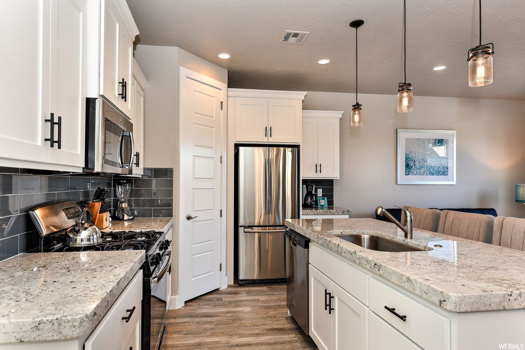 kitchen featuring hardwood floors, stainless steel dishwasher, refrigerator, microwave, gas range oven, white cabinets, light granite-like countertops, and pendant lighting