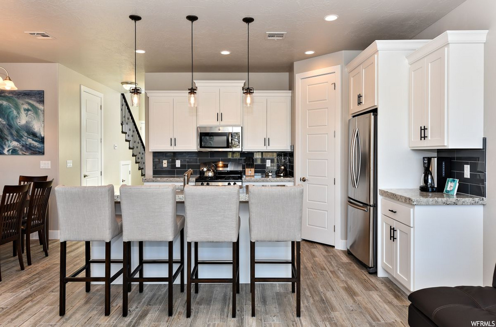 kitchen featuring a breakfast bar area, wood-type flooring, microwave, refrigerator, range oven, pendant lighting, light countertops, and white cabinets