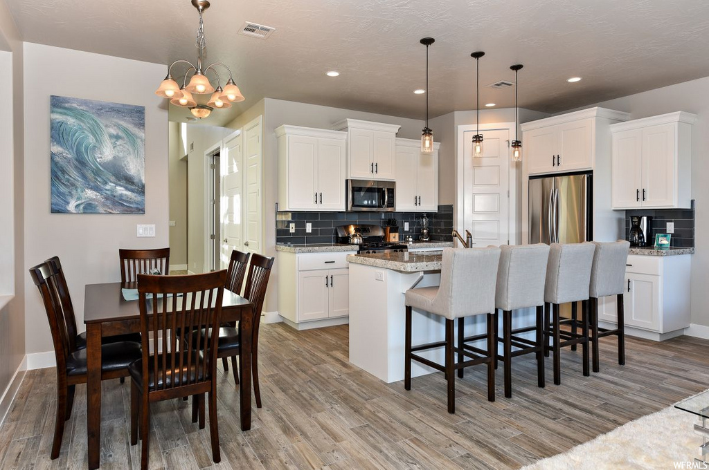 kitchen with hardwood floors, a breakfast bar, stainless steel refrigerator, microwave, range oven, light countertops, pendant lighting, and white cabinets