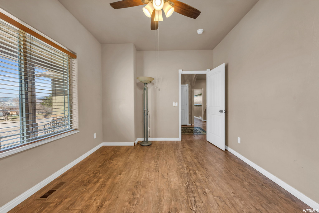 Wood floored empty room with natural light and a ceiling fan