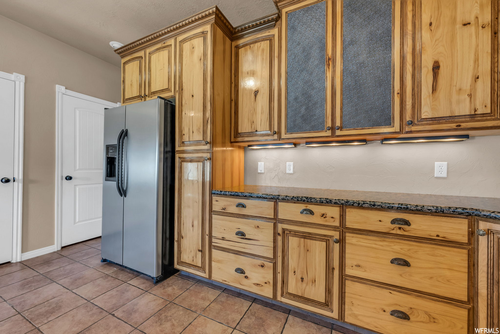 Kitchen with refrigerator, light tile floors, brown cabinetry, and dark countertops