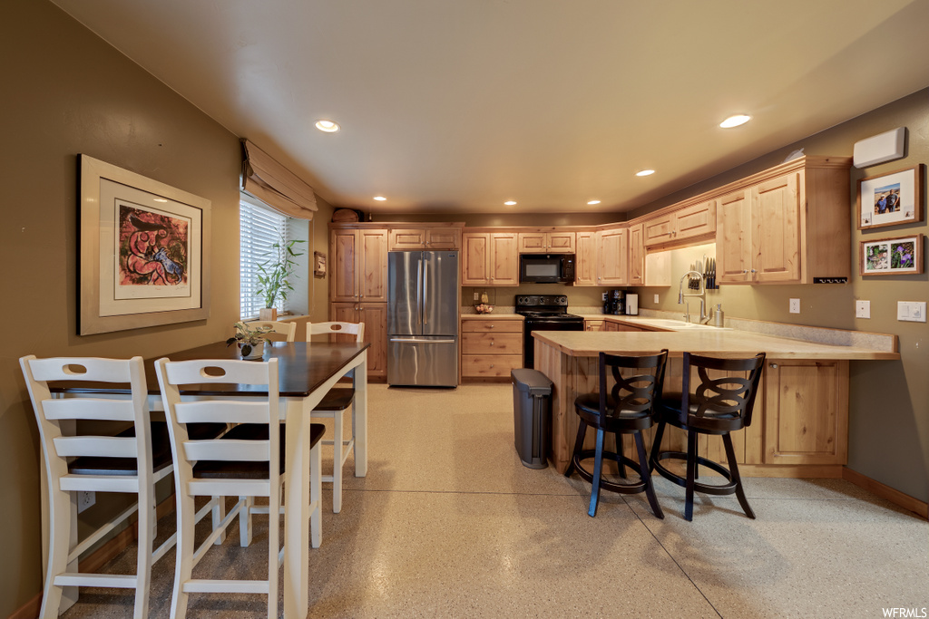 kitchen featuring natural light, a breakfast bar, refrigerator, microwave, range oven, light flooring, and light countertops