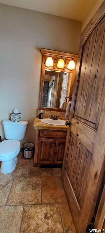 half bathroom with tile floors, mirror, toilet, and vanity