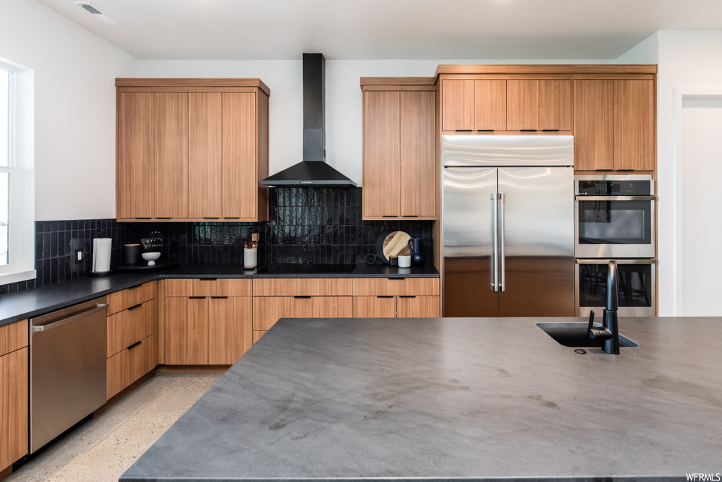 kitchen featuring exhaust hood, stainless steel dishwasher, double oven, refrigerator, brown cabinets, and light flooring