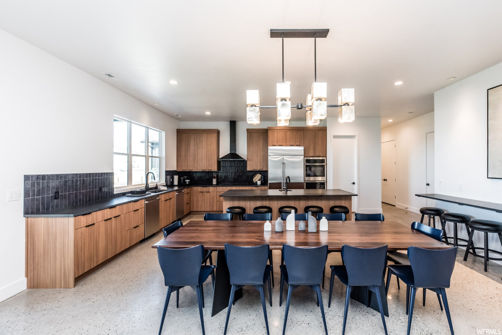 kitchen with natural light, a breakfast bar, stainless steel appliances, extractor fan, dark countertops, brown cabinets, and light flooring