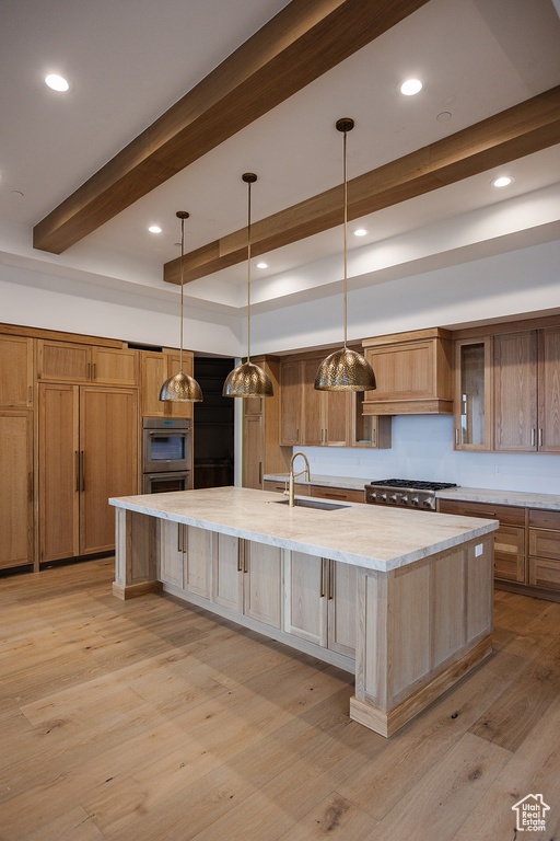 Kitchen with light hardwood / wood-style floors, a center island with sink, hanging light fixtures, custom range hood, and sink