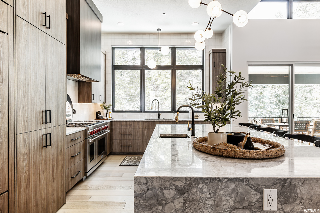 kitchen featuring a healthy amount of sunlight, gas range oven, stainless steel finishes, light flooring, granite-like countertops, and kitchen island sink