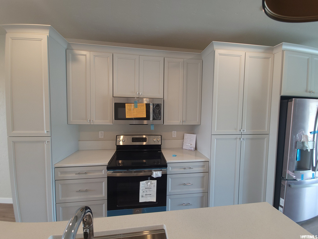 Kitchen featuring electric range oven, microwave, refrigerator, white cabinets, and light countertops