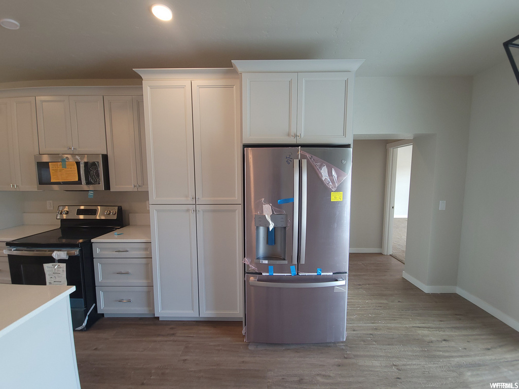 Kitchen featuring wood-type flooring, electric range oven, microwave, stainless steel refrigerator, light countertops, and white cabinetry