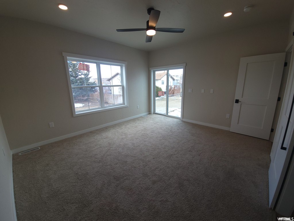 Carpeted empty room featuring a ceiling fan and natural light