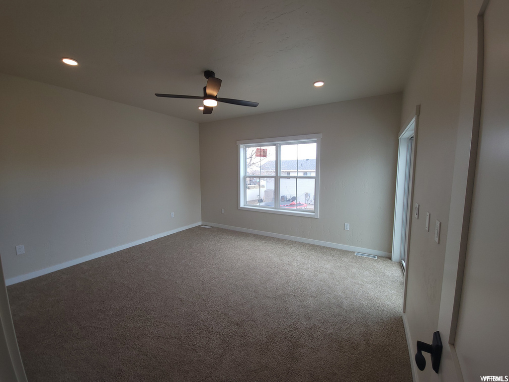 Empty room featuring a ceiling fan, carpet, and natural light