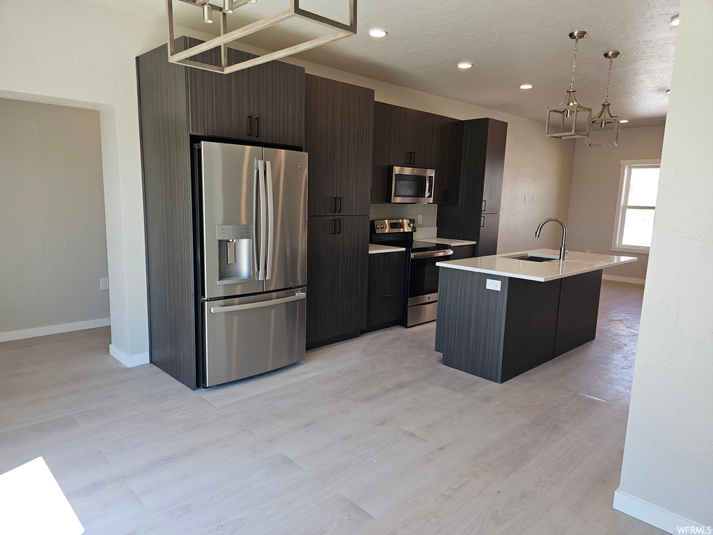 Kitchen with dark brown cabinets, light hardwood floors, and appliances with stainless steel finishes