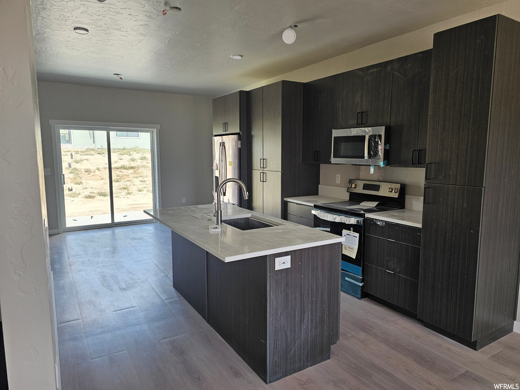 Kitchen featuring dark brown cabinets, appliances with stainless steel finishes, light hardwood floors, and light countertops